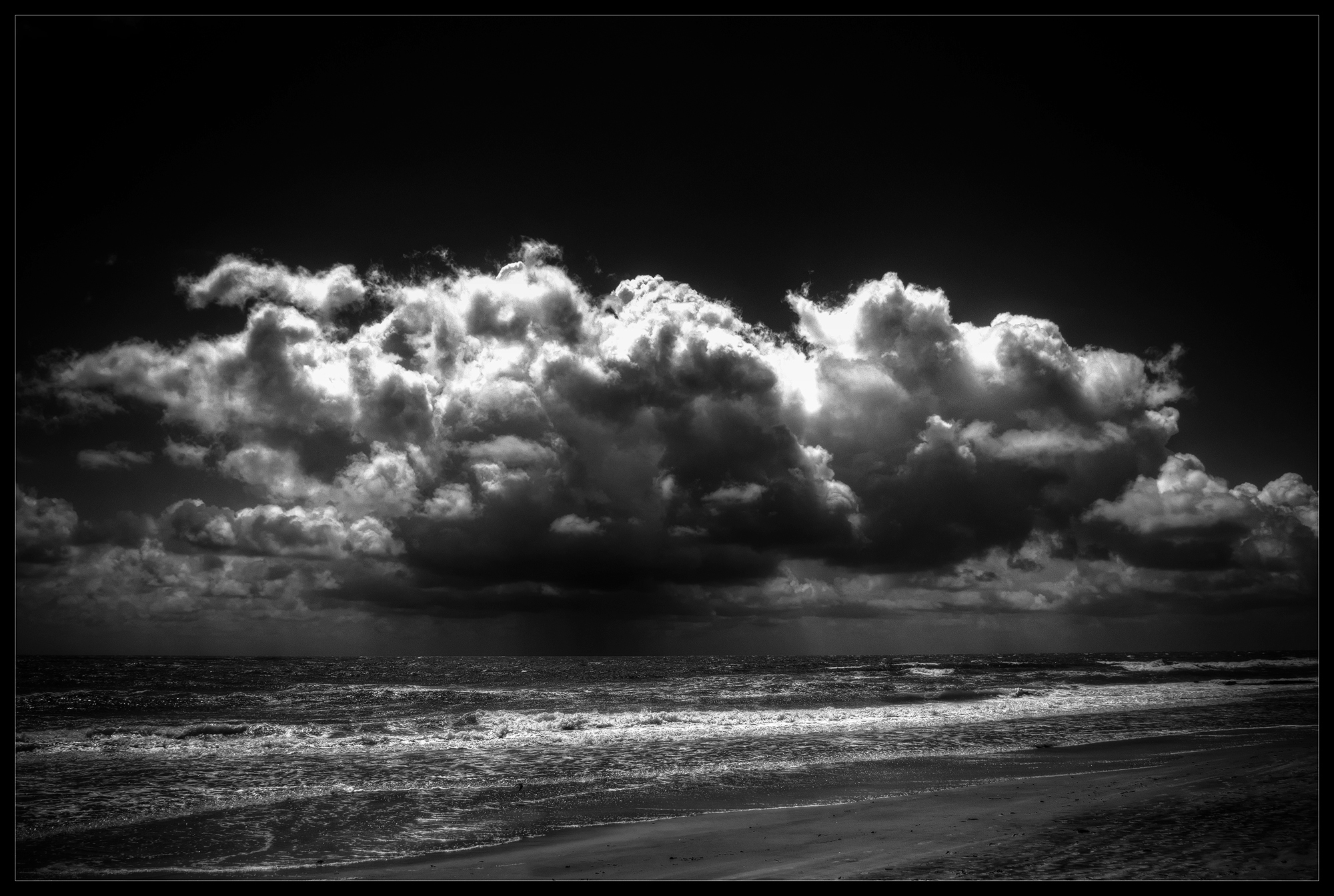 A black-and-white photograph of a stormy beach with clouds.